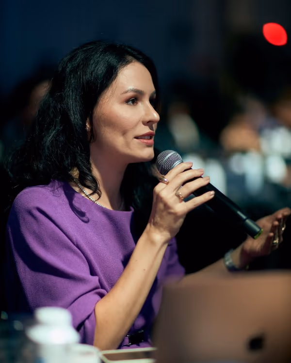 Andressa Ducosta com o microfone, falando à plateia durante um evento